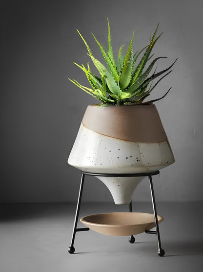 HongLuo Artisan Planters Family features a modern two-tone ceramic planter with minimalist stand design. Tapered white and beige pot with speckled texture sits elegantly on black metal tripod legs, displaying a vibrant aloe plant. Includes decorative catch plate beneath.