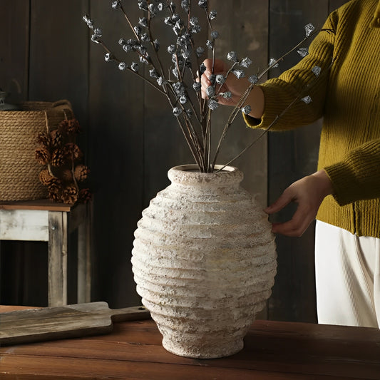 Gu Yun Antique Family vintage-style textured ceramic vase in weathered white with horizontal ribbed pattern, displaying delicate white floral stems, photographed on wooden surface with mustard yellow sleeve visible arranging flowers